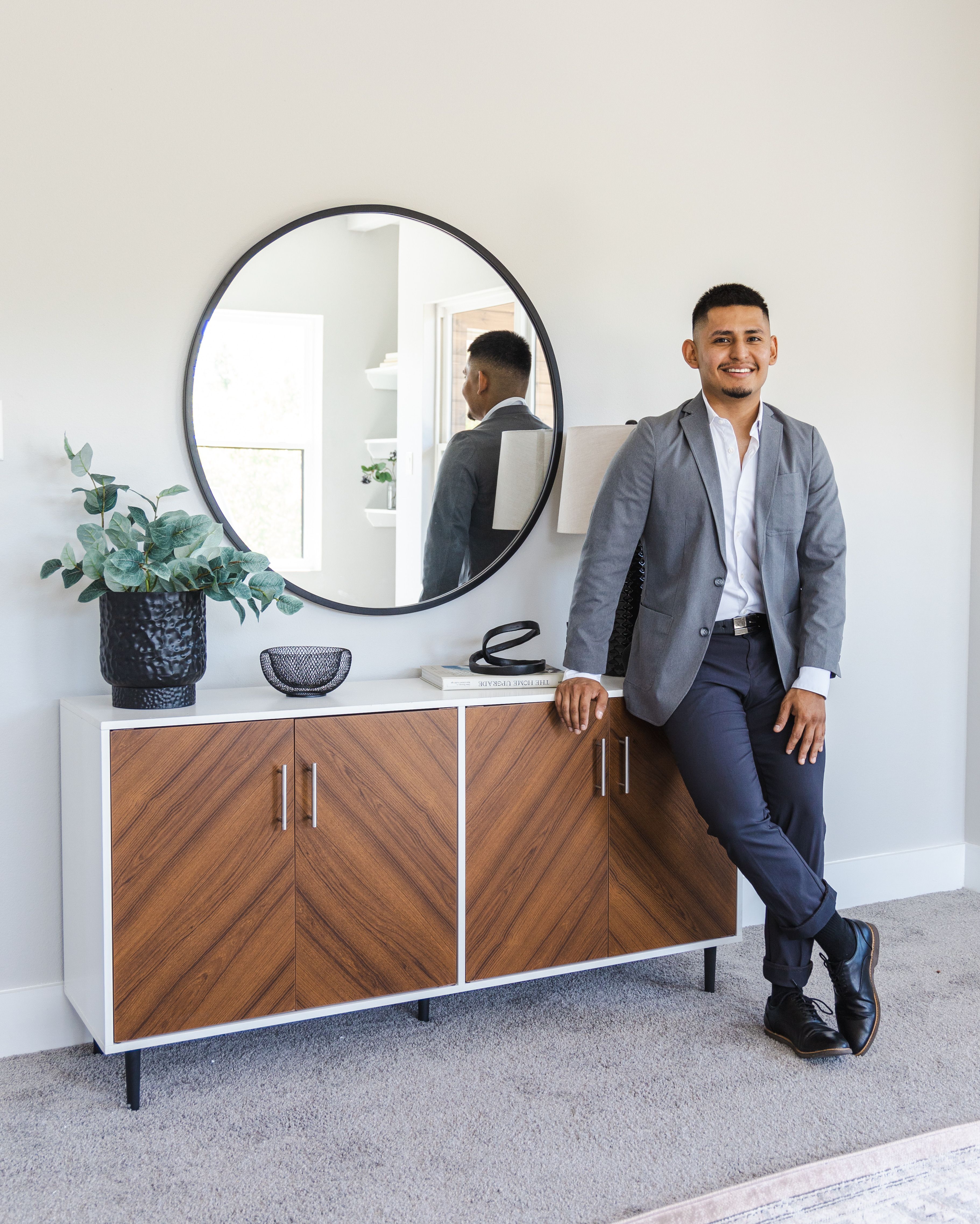 Confident man in a suit leaning by a cabinet with mirror reflection.