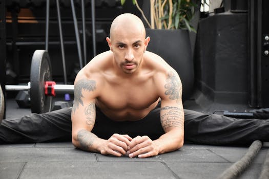 Bald man with tattoos stretching in gym, showcasing strength and flexibility.