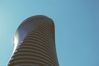 一座现代化的摩天大楼与一座弯曲的建筑在清澈的蓝天下拔地而起，展现了未来主义的设计