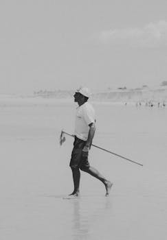 Black and white photo of a man with a fishing rod strolling along the Canoa Quebrada coast in Brazil.