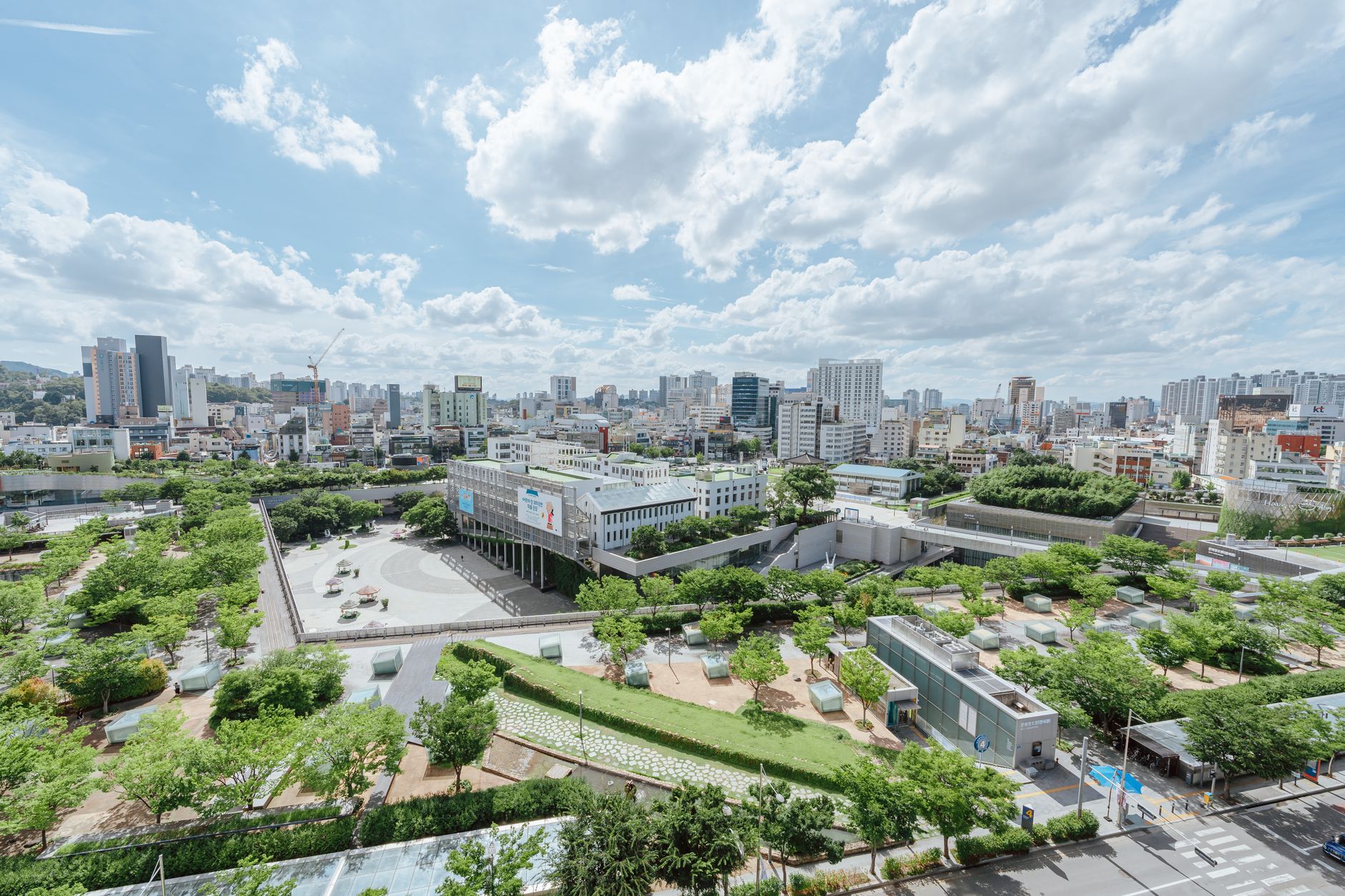 Aerial view of lush urban gardens and sprawling cityscape under a bright summer sky.