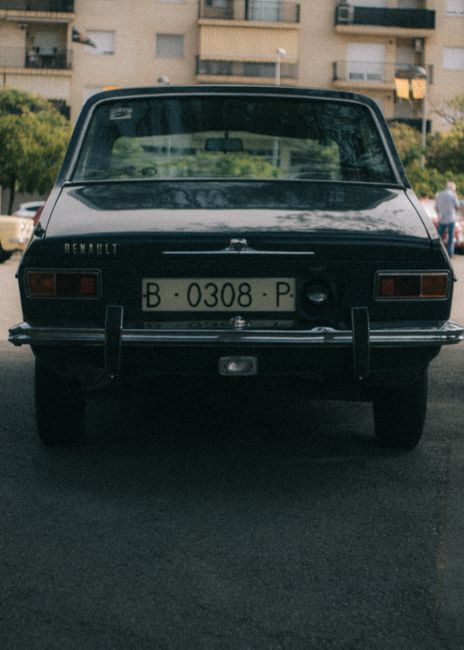 Fotomural Vista trasera de un coche clásico Renault aparcado en las bulliciosas calles de Barcelona, capturando el encanto vintage de la ciudad.