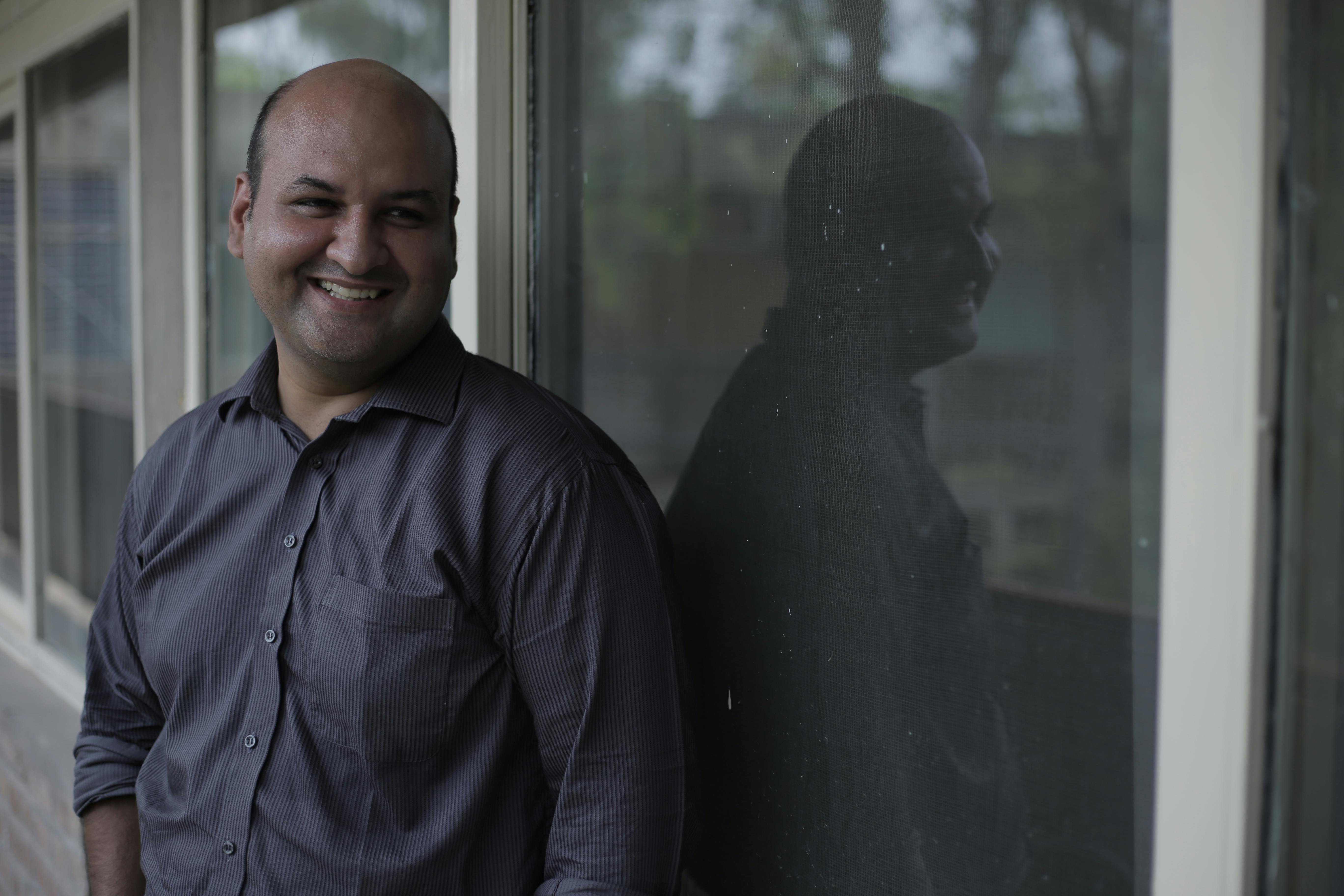 Bald man smiling while leaning against a window in Lahore, Pakistan.