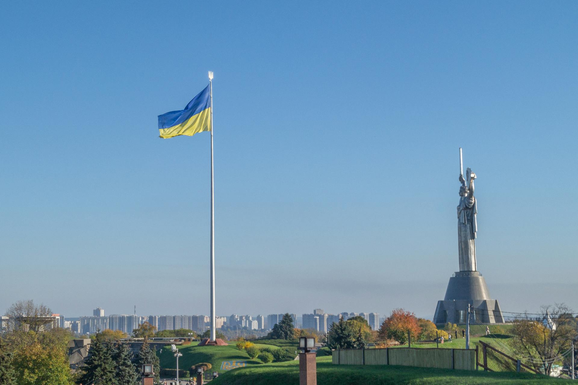 The Motherland Monument and national flag in Kyiv, Ukraine showcasing urban landscape and clear sky.