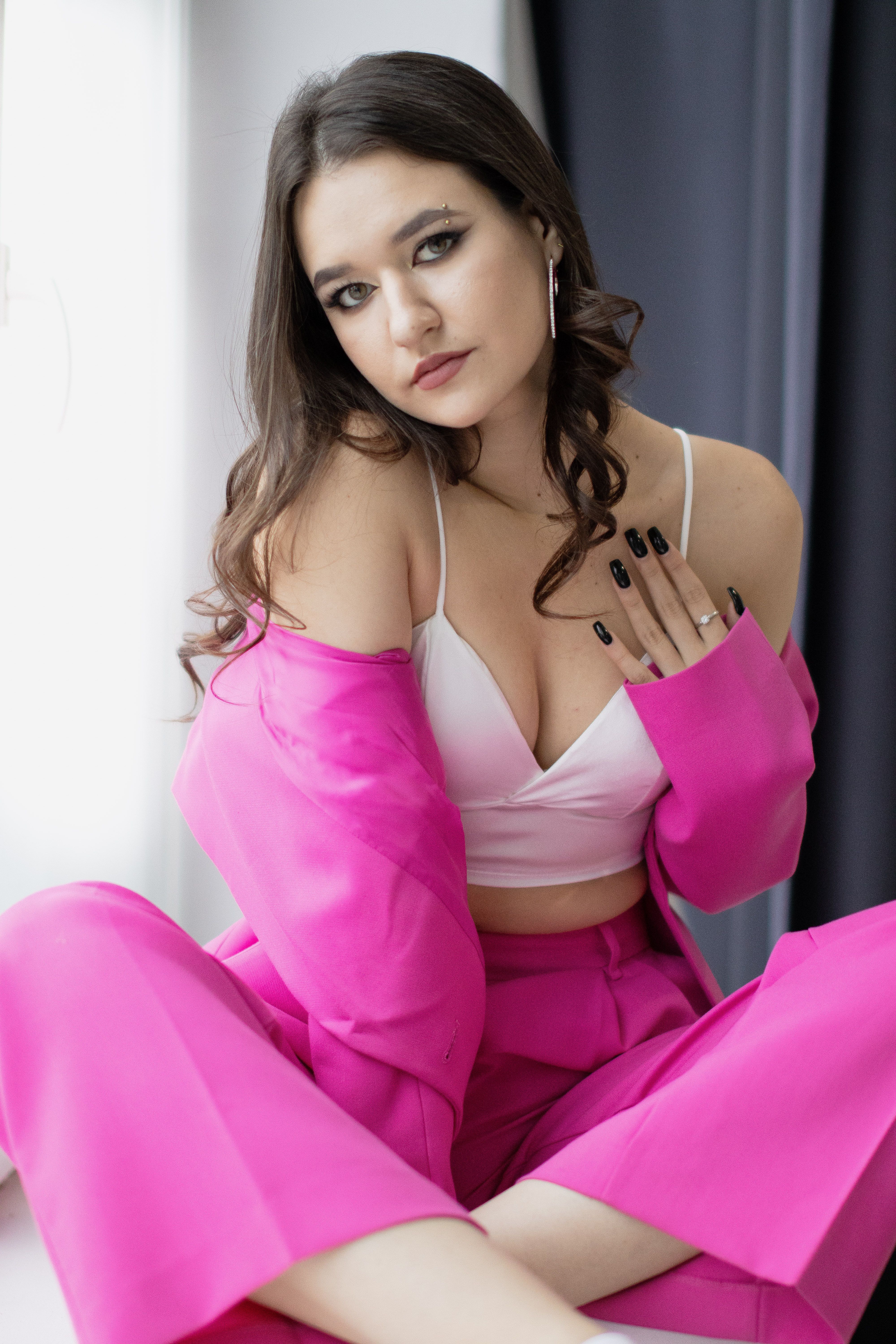 Young woman in vibrant pink suit with bralette posing elegantly indoors.