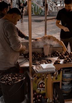 Busy street vendor preparing hot roasted chestnuts in a bustling urban setting.