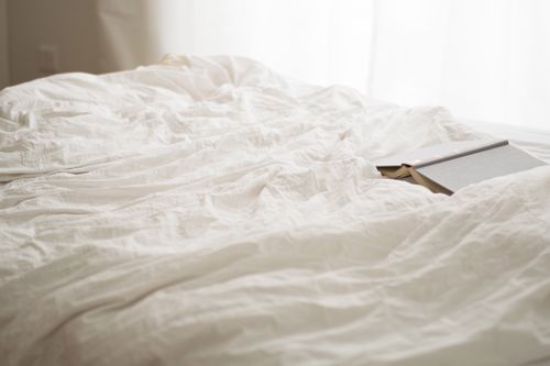 Free A serene bedroom scene with soft white sheets and a book, evoking relaxation and calm. Stock Photo