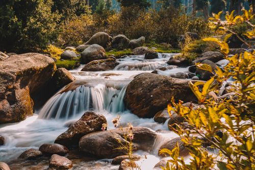 Free A serene river cascades over rocks surrounded by vibrant autumn foliage. Stock Photo