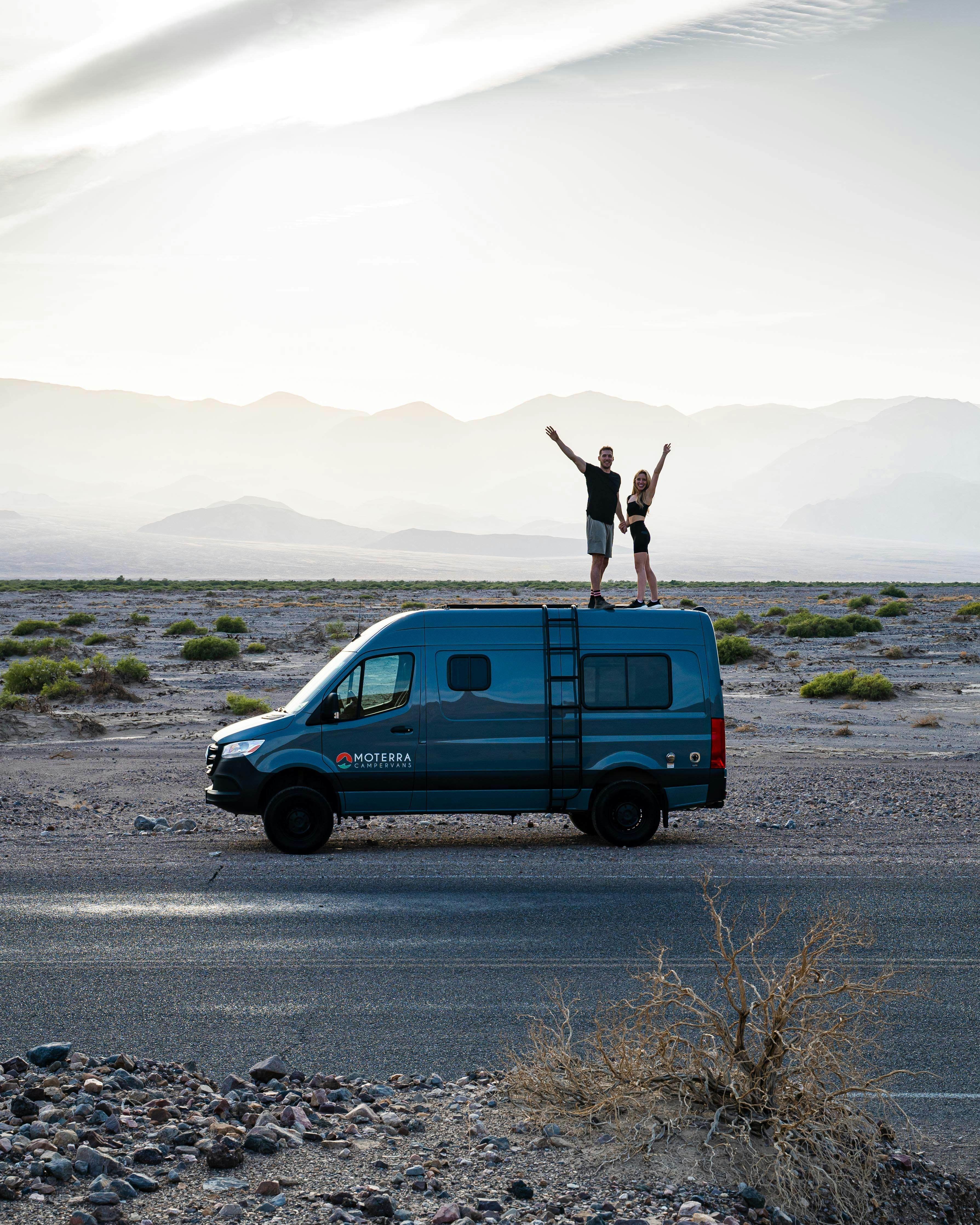 Couple standing on camper van in Death Valley desert, embracing van life.