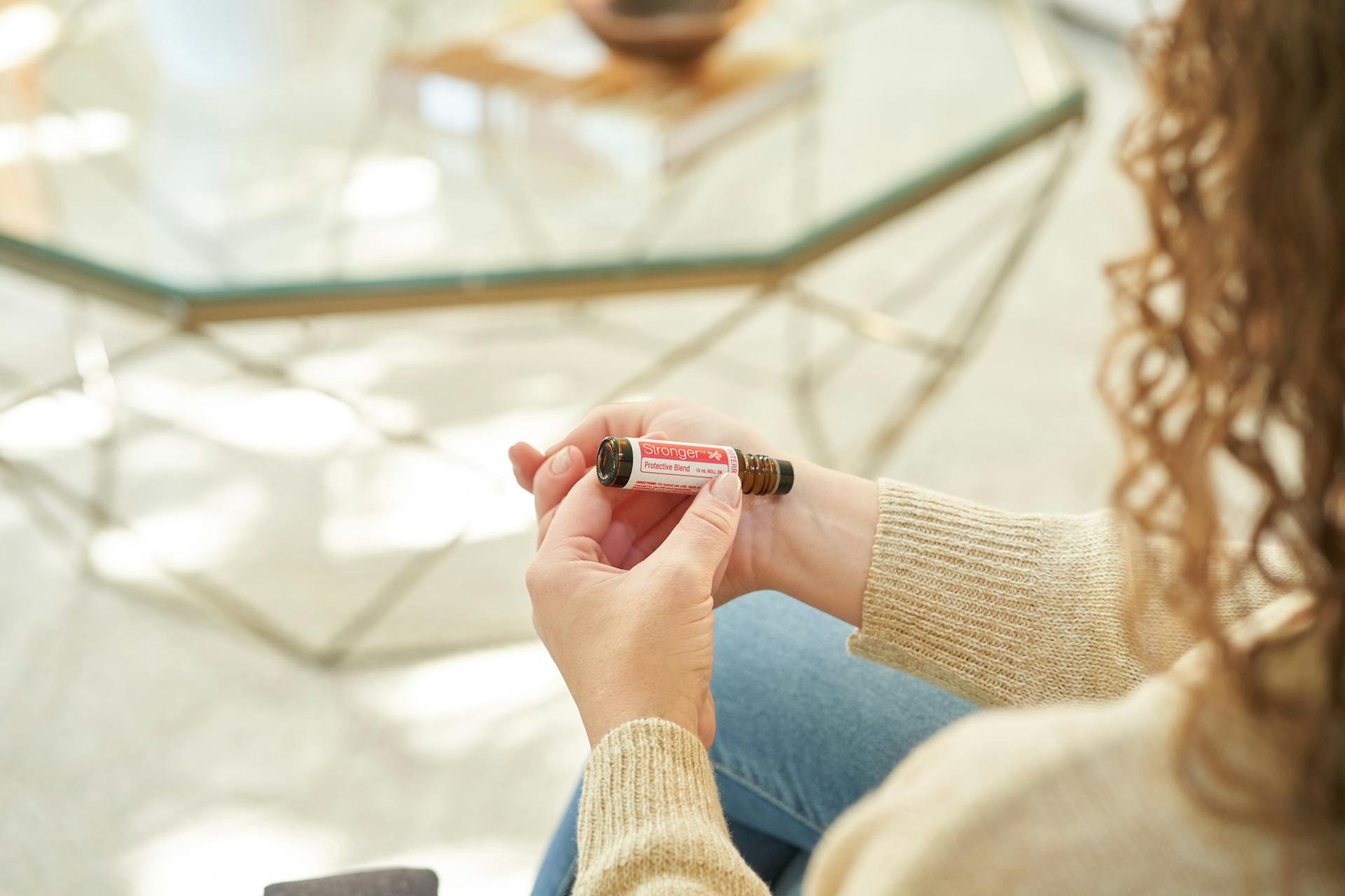 Close-up of a woman holding an essential oil roller in a relaxed indoor environment.