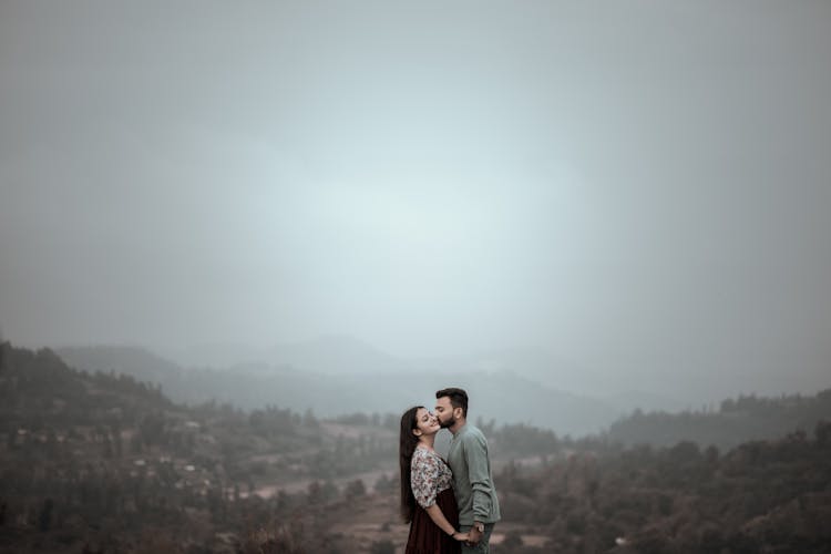 Couple Kissing On Top Of Hill Under Cloudy Sky