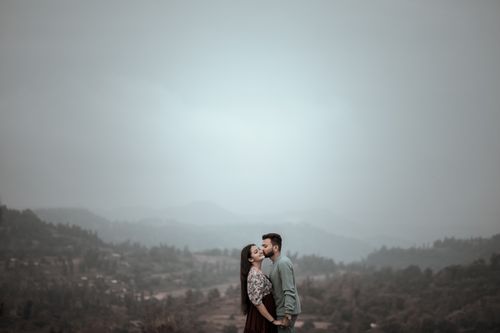 Free A couple shares a tender kiss on a misty hillside under a cloudy sky, full of romance and affection. Stock Photo