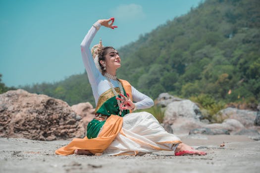 Odissi dancer performs beautifully, seated outdoors on a sandy landscape.