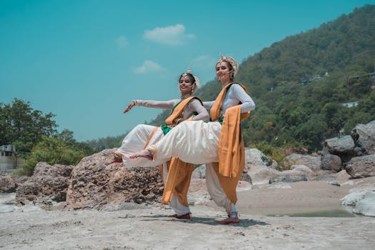 Two Odissi dancers gracefully performing on a sunny beach in Puri, India.