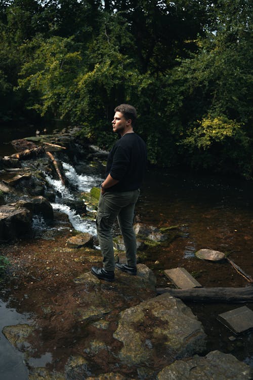 A Man in Black Long Sleeves Standing on a Rocky River