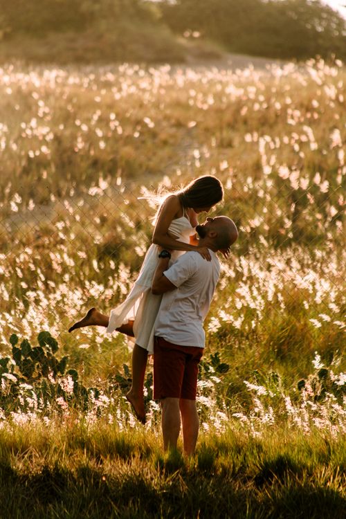 Free A couple sharing an intimate moment in a sunlit grassy field, symbolizing love and togetherness. Stock Photo