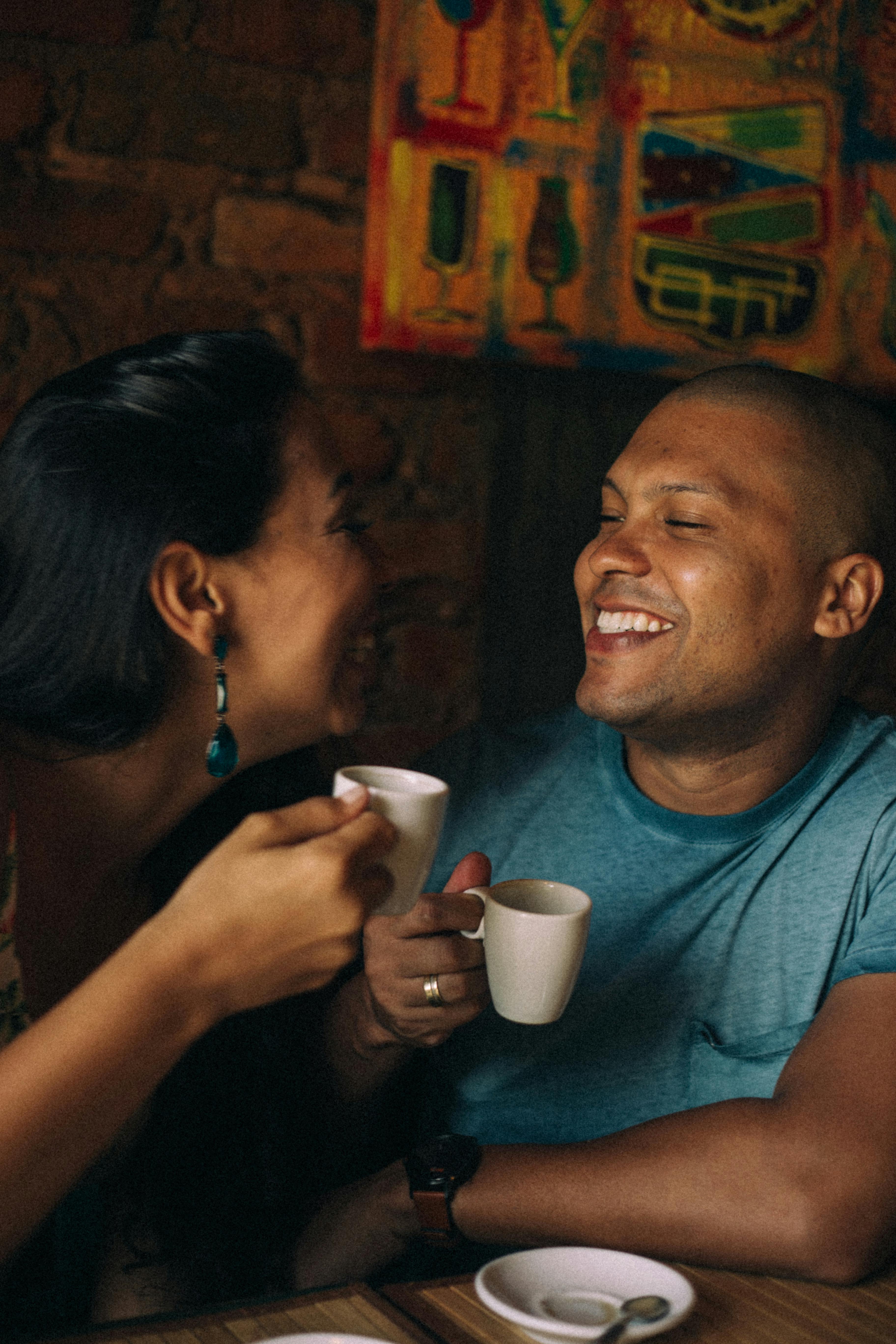 A joyful couple shares a warm moment over coffee in an intimate cafe environment.