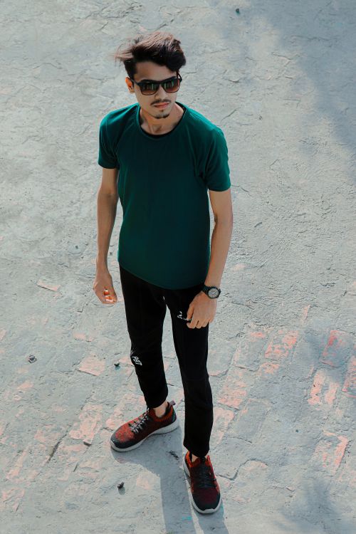 Free Casual young man in a green shirt and sunglasses standing outdoors with a confident pose. Stock Photo