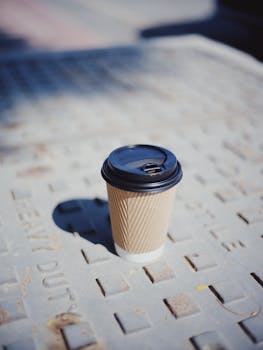 A single disposable coffee cup casting a shadow on the sidewalk.