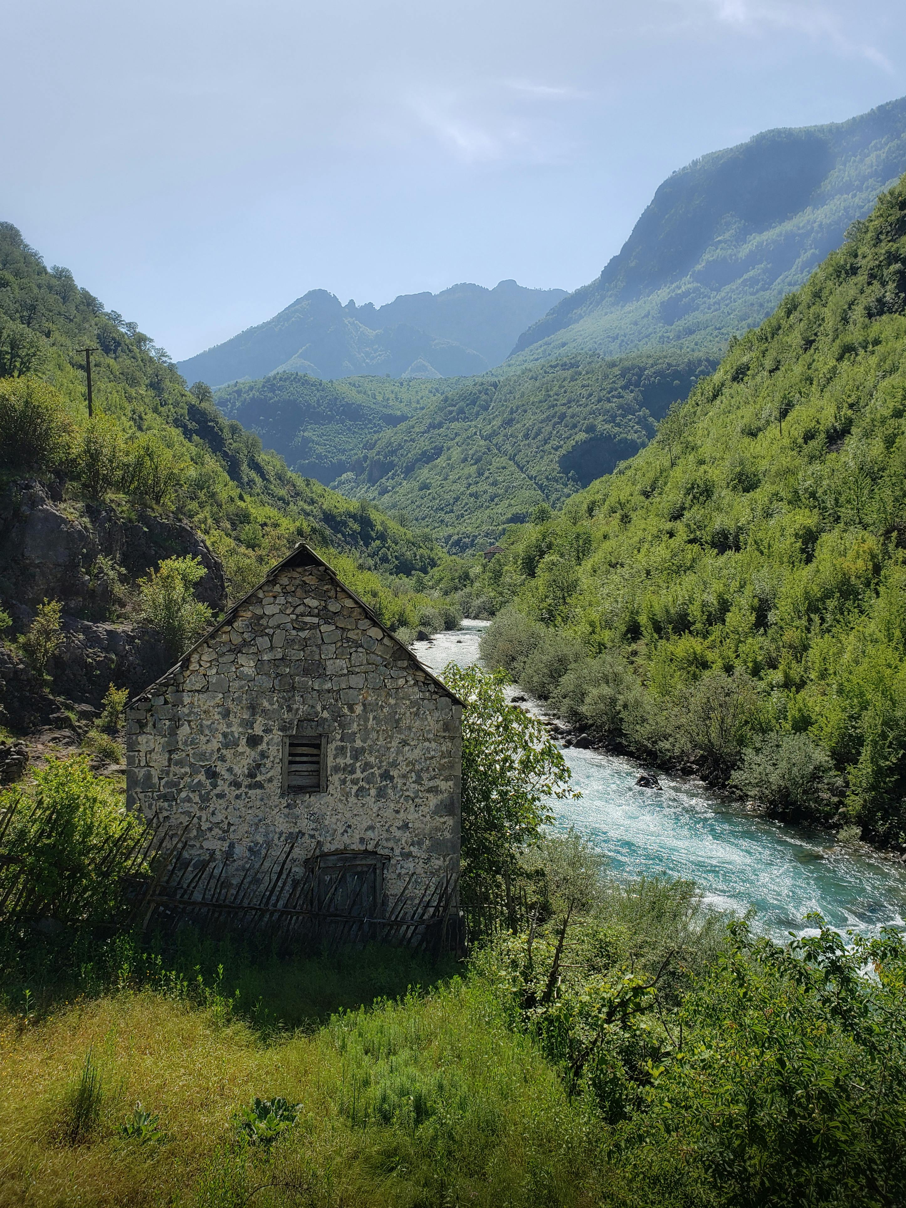 A tranquil stone house by a rushing river in the lush mountainous region of Tamarë, Albania.