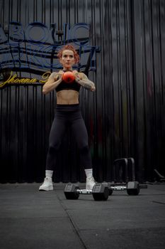 Tattooed woman exercises with kettlebell at a gym in Ciudad de México, achieving fitness goals.