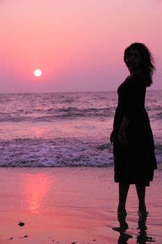 Silhouette of a woman standing on the beach during a vibrant sunset.