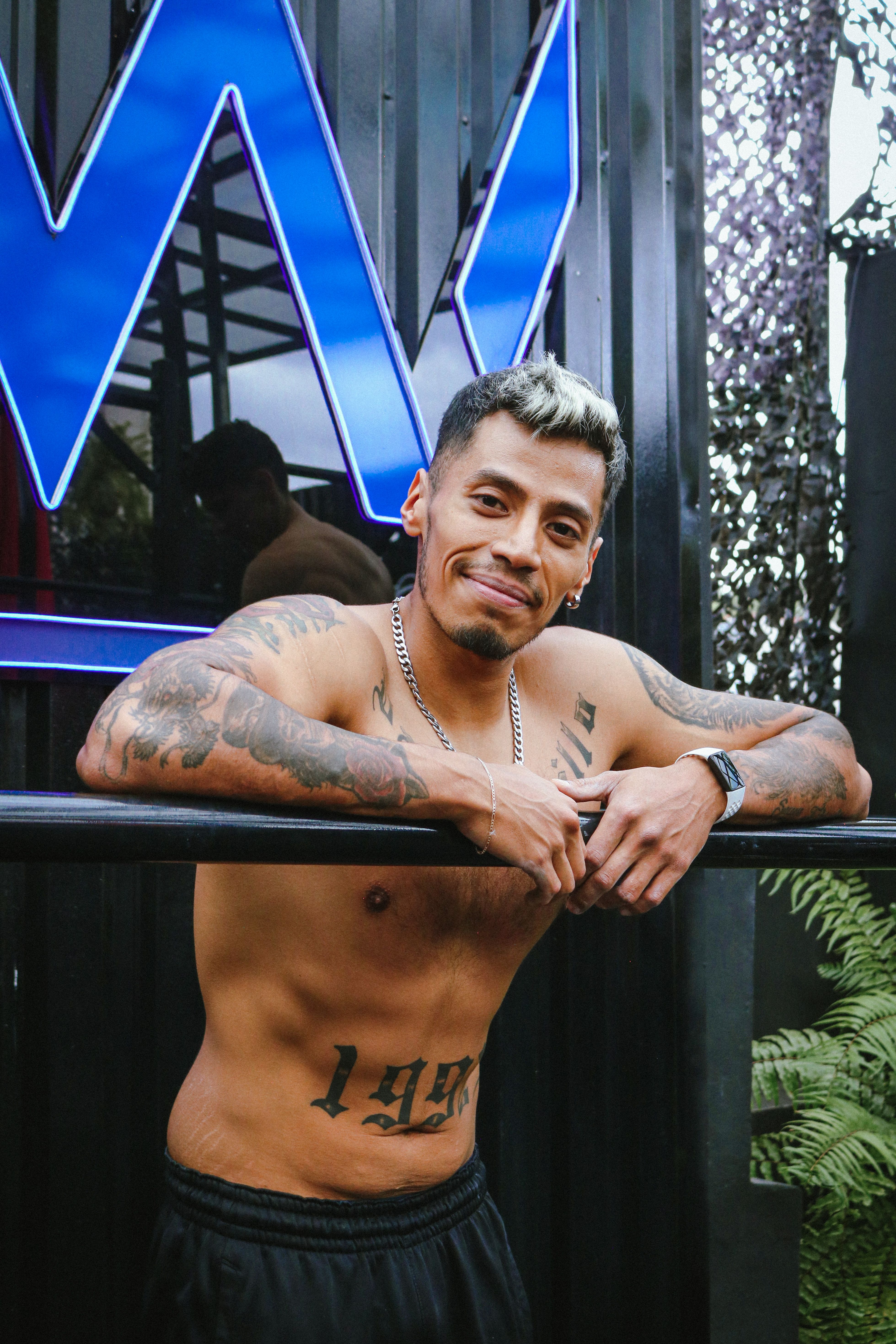 Smiling tattooed man leaning on bar outdoors in Mexico City.