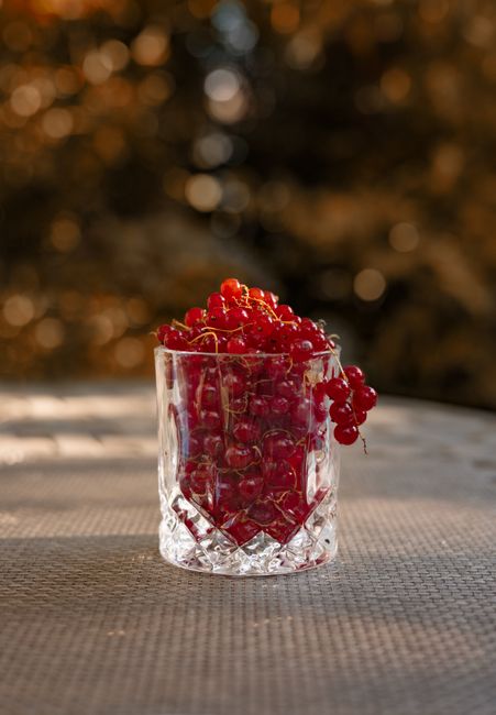 A crystal glass brimming with vibrant redcurrants on a textured table outdoors.