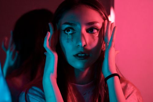 Free A woman gazing into a mirror with glitter tears, reflecting dramatic emotions in neon lighting. Stock Photo
