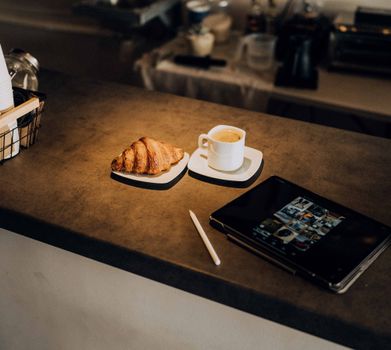 Cozy café setting featuring a croissant, coffee, and tablet on a countertop. Perfect for lifestyle and technology themes.
