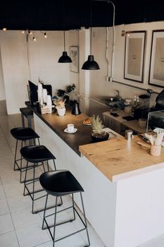 A stylish and minimalistic café interior featuring a wooden counter, black stools, and hanging lamps.