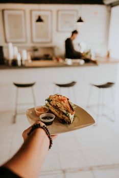 Close-up of a gourmet sandwich held by a hand in a chic minimalist cafe setting.