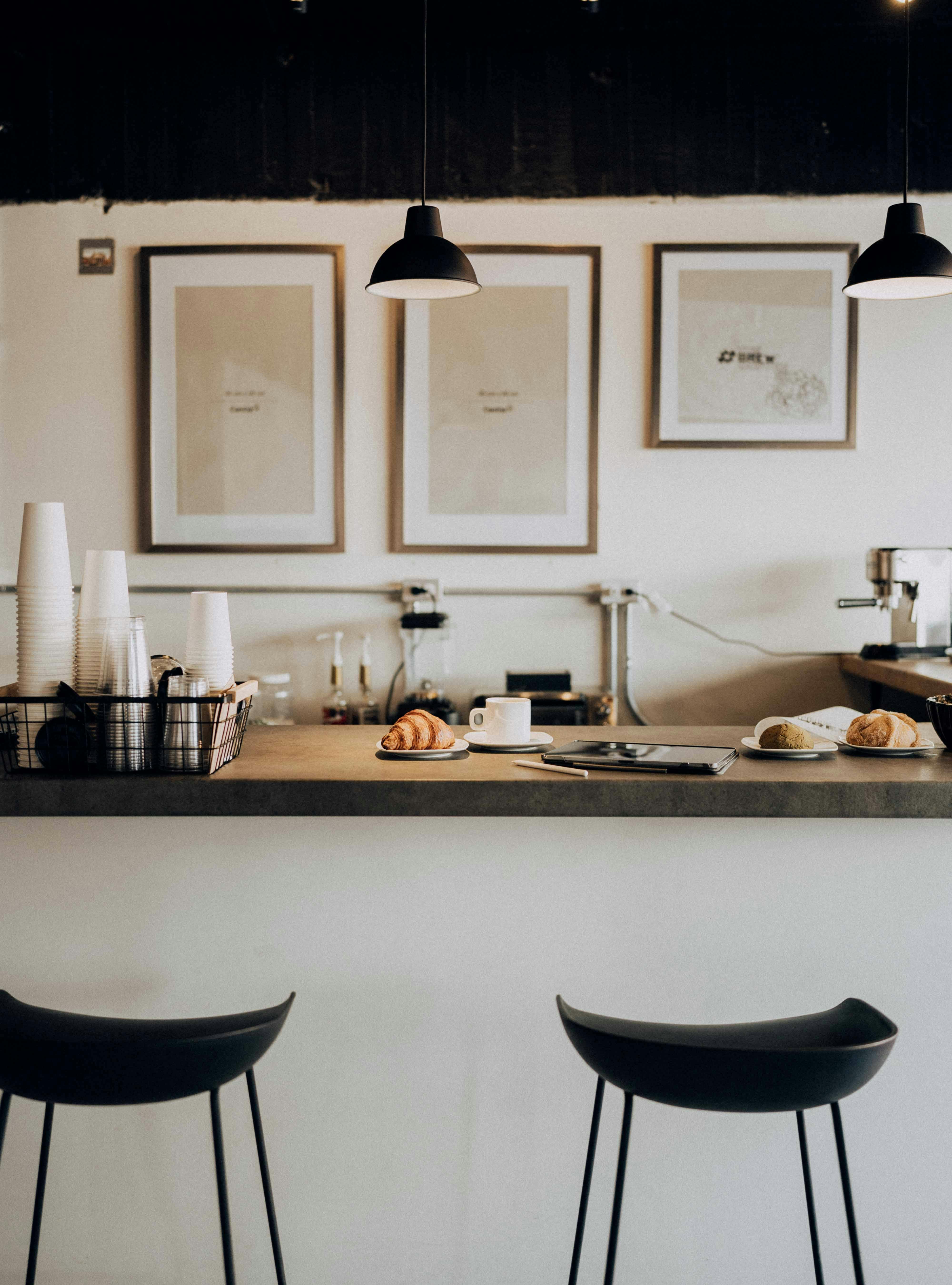 Cozy café counter with stools, pastries, and framed art on the wall, showcasing minimalist design.