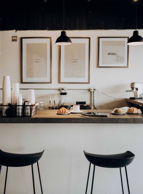 Cozy café counter with stools, pastries, and framed art on the wall, showcasing minimalist design.