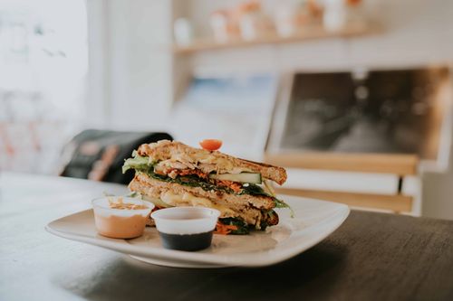 Free Close-up of a gourmet sandwich with dipping sauces on a white plate, captured in a cozy cafe setting. Stock Photo