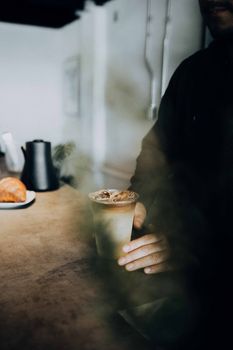 A cozy indoor cafe setting with a person holding an iced coffee and a croissant on the table.