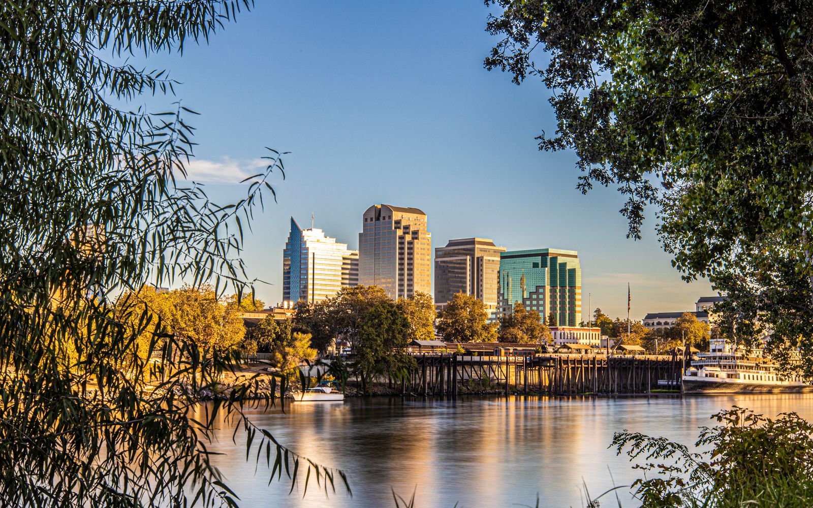 The Sacramento skyline at sunset, reflected in the river and framed by trees