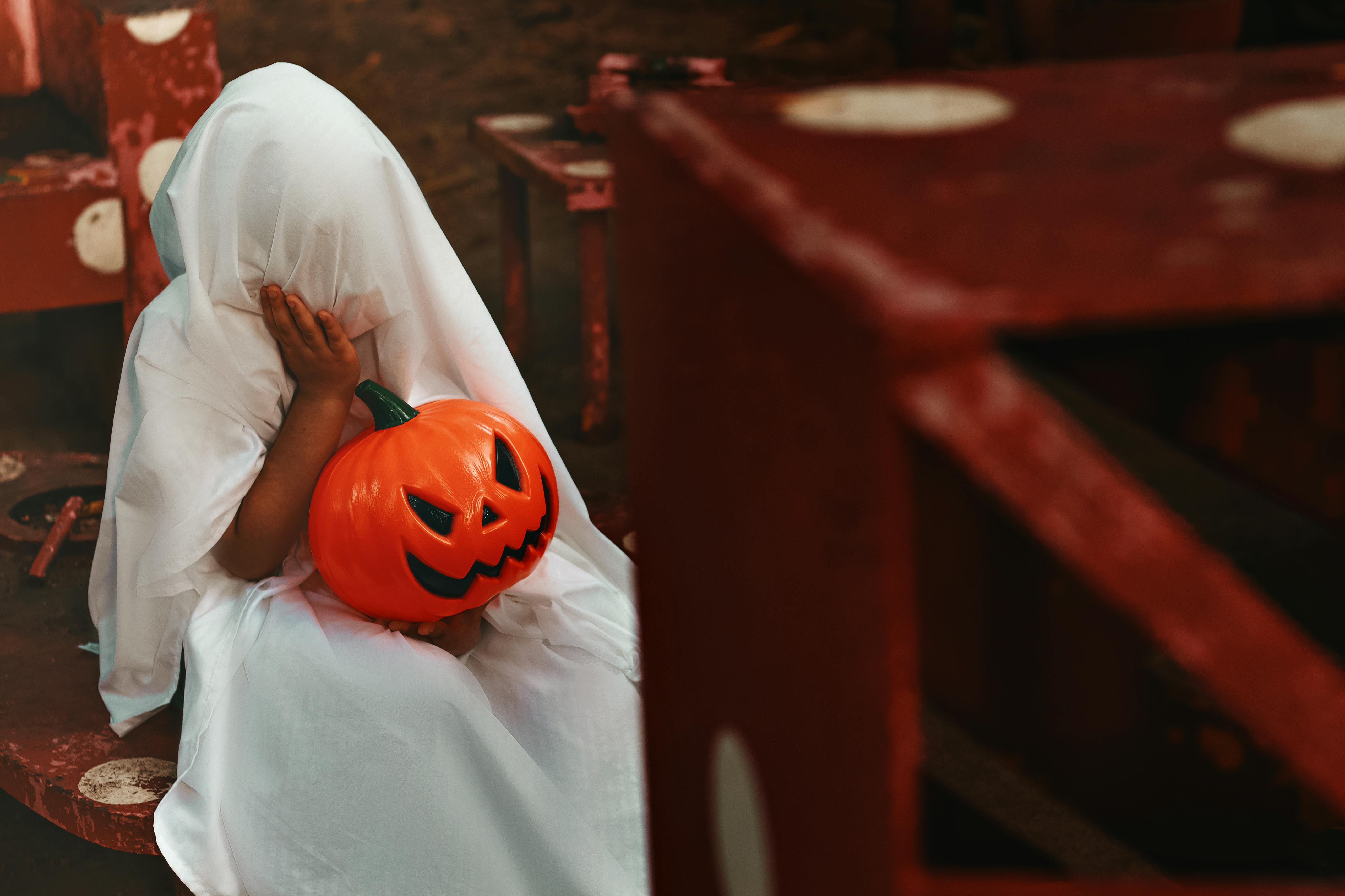 person covered with white blanket holding a jack o lantern