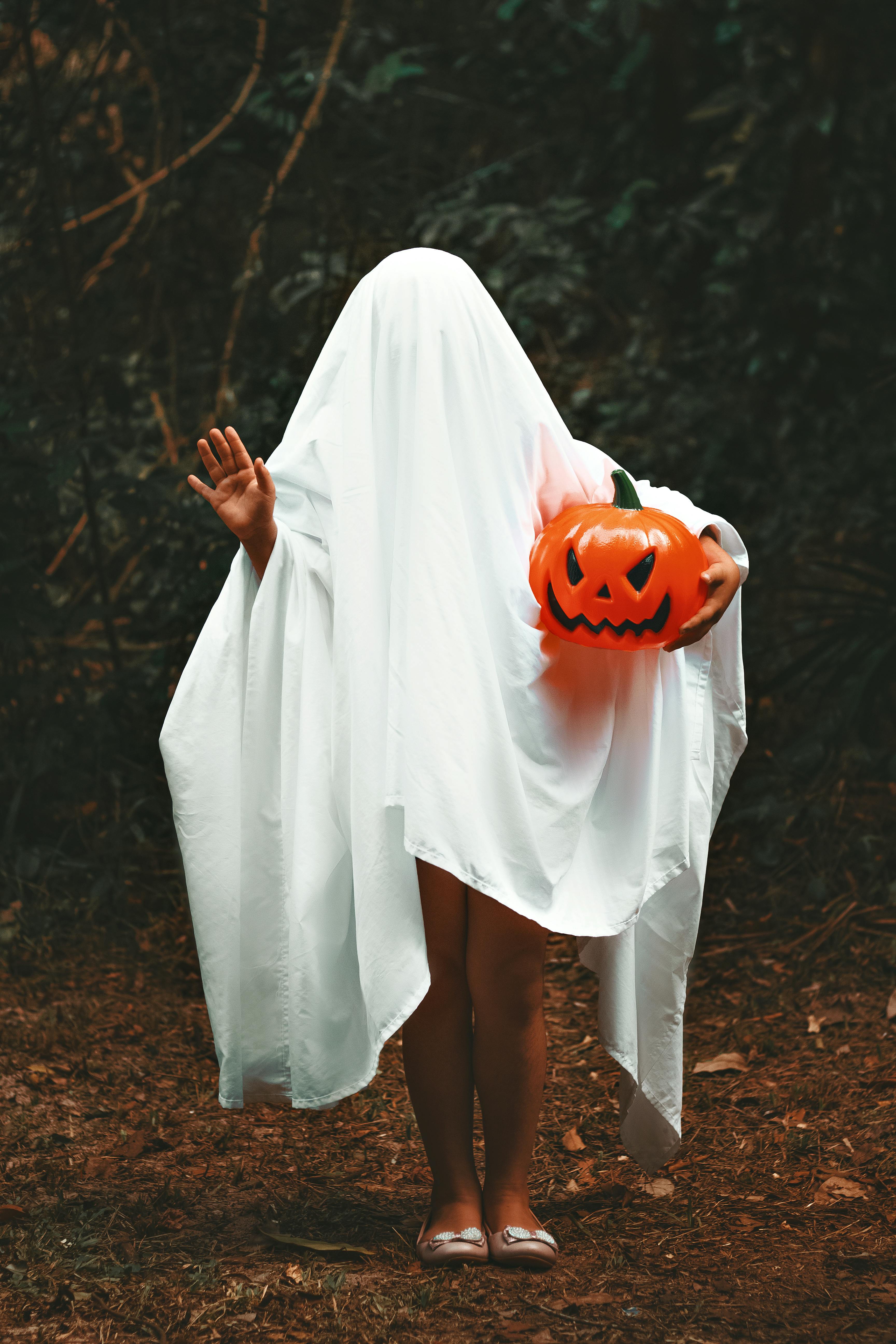 woman covered in white blanket holding a jack o lantern