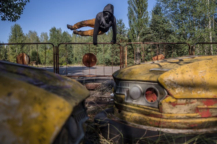 Man Jumping On Brown Metal Fence Towards Two Yellow Bump Cars