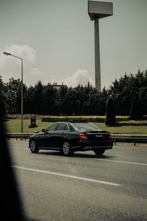 Free A sleek black sedan travels on an Istanbul road, surrounded by greenery and urban infrastructure. Stock Photo