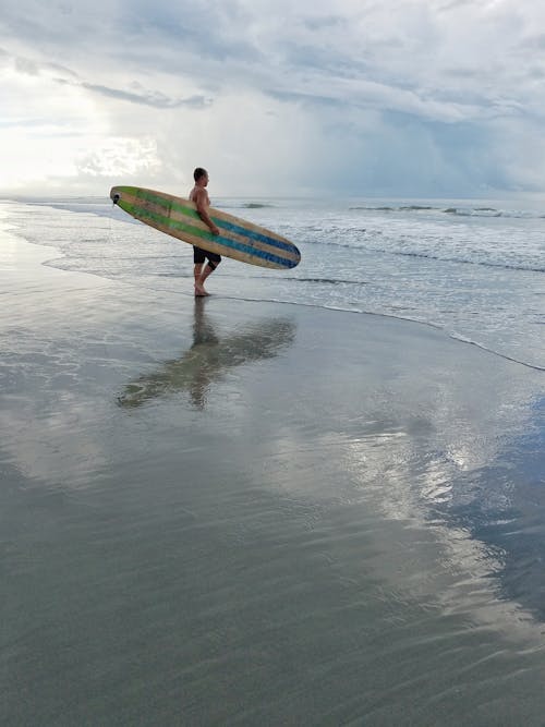 Мужчина держит доску для серфинга, глядя на океан
