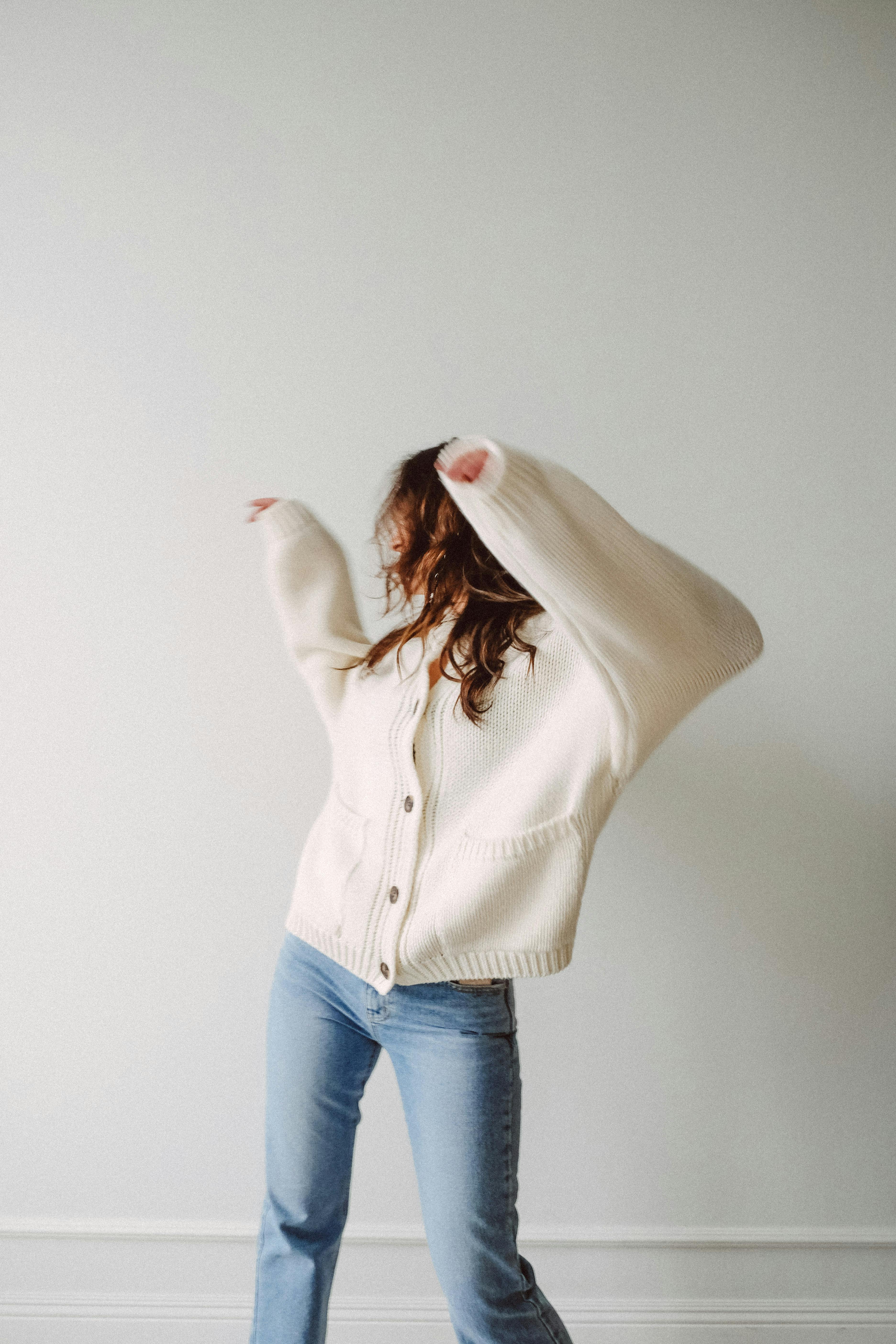 woman wearing white sweater and blue jeans moving against white wall