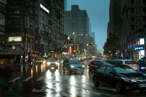 Free A bustling city street in the rain with cars and bright lights at dusk. Stock Photo