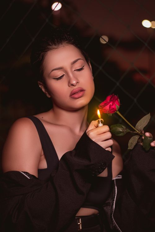 Free A moody portrait of a woman holding a lit lighter next to a red rose at night. Stock Photo