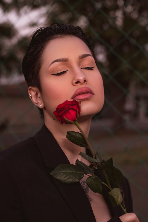 Free Portrait of a woman with eyes closed holding a red rose, exuding elegance and tranquility. Stock Photo