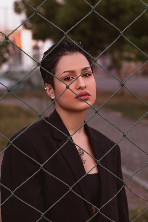 Free Portrait of a fashionable woman with short hair and black blazer behind a chain link fence. Stock Photo