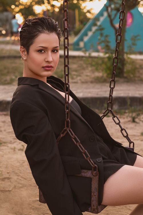 Free Confident woman in a black blazer sits on a swing in the park, capturing a dynamic outdoor portrait. Stock Photo