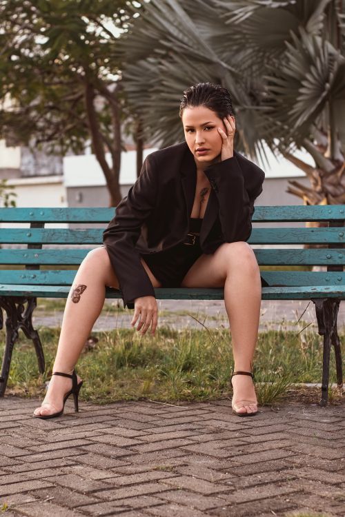 Free Stylish woman with short hair in a black blazer sitting confidently on a park bench. Stock Photo