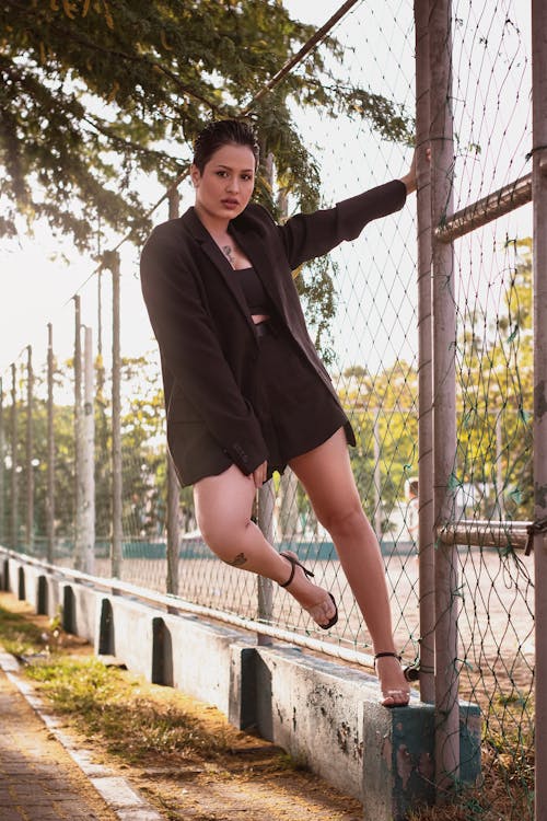 Woman in Black Blazer Standing Beside a Chain Link Fence